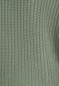 Tessuto in maglia di un verde tenue, caratterizzato da un design a coste testurizzato con cuciture uniformi e una densità media.
