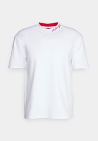 Bílý krátký rukáv tričko vyrobené z bavlny, které má vysoký výstřih s červenou vnitřní vrstvou a červeně vyšívané logo na límci.