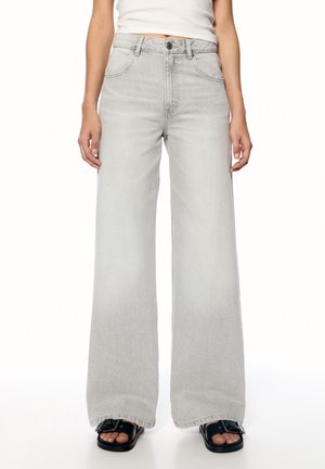Lysegrå brede jeans lavet af denim, med høj talje, klassisk fem-lomme design og rå kant. Parret med sorte slidesandaler.