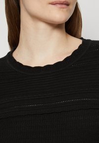 Maglione nero con un design a coste testurizzato e scollatura a ondine. Il tessuto sembra leggero con dettagli orizzontali sottili.