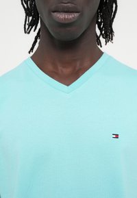 Γαλάζιο βαμβακερό t-shirt με v-λαιμόκοψη, που διαθέτει ένα μικρό κεντημένο λογότυπο με κόκκινες, λευκές και μπλε λεπτομέρειες στο στήθος.