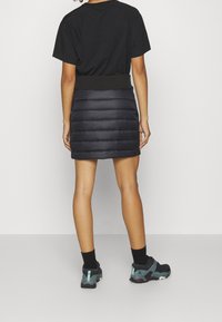Camiseta negra de manga corta combinada con una falda corta y abullonada de color azul oscuro a la altura de la rodilla. La falda cuenta con una cinturilla acanalada y costuras horizontales. Se llevan zapatillas negras.