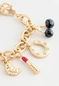 Zlatý kovový náramek s přívěsky, které zahrnují černou třešeň, croissant, rtěnku a podkovu, zdobené diamantovými akcenty a texturovaným povrchem.