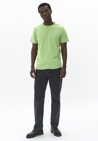 Camiseta de algodón verde con cuello redondo, combinada con jeans rectos de color gris oscuro y zapatos marrones. Diseño sencillo, textura suave y ajuste casual.