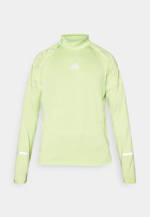 Heledad roheline pikkade varrukatega spordipluus, millel on valge logo ja peegeldavad aktsendid mansettidel. Valmistatud tekstuurilisest, hingavast materjalist.