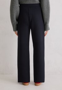 Granatowe spodnie o szerokich nogawkach i wysokim stanem, z bocznymi szwami i gładką fakturą. Połączone z szarym, prążkowanym swetrem i czerwonym obuwiem.