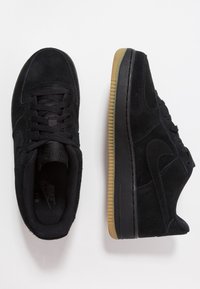 Sneakers in suede nero con suola in gomma, caratterizzati da un motivo testurizzato e lacci tono su tono. Punta rotonda, design minimalista, senza branding visibile.