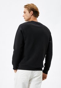 Zwart sweatshirt met een ronde halslijn en ribbed manchetten. Beschikt over een gladde textuur en raglanmouwen, gecombineerd met lichte broek.