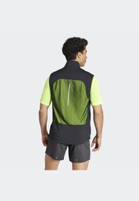 Schwarze und grüne leichte Sportweste mit hohem Kragen, Netzrückenpaneel, reflektierendem Streifen und kurzen Ärmeln, kombiniert mit dunklen Shorts.