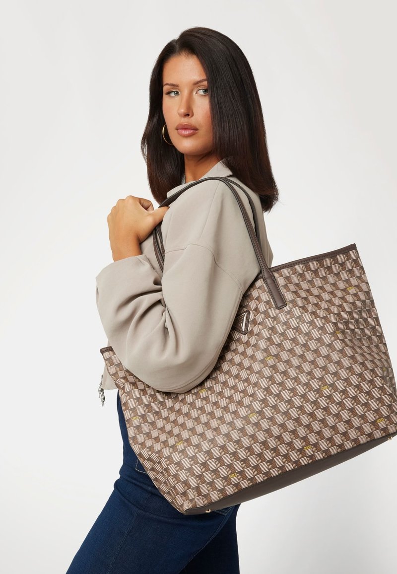 Grand sac fourre-tout avec un motif à damier marron et beige, texture lisse et longues bandoulières. Des accents dorés subtils viennent embellir le design.
