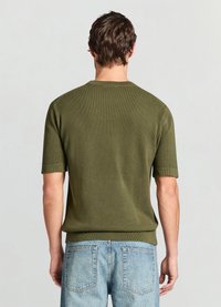 Pull court en tricot vert foncé à manches courtes avec un motif texturé, col rond et poignets côtelés. Associé à un jean en denim bleu clair.