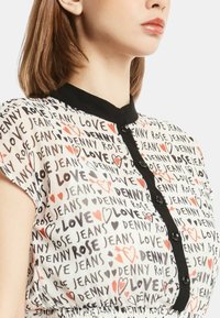 Blusa bianca con colletto e bottoni neri, caratterizzata da un motivo ripetuto di testo nero e rosso con le scritte "Denny Rose," "Jeans," e cuori.