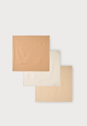 Trois carrés de tissu pliés en beige, crème et marron clair disposés en chevauchement sur un fond blanc.