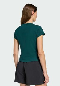 Teal short-sleeve t-shirt with a fitted design, ribbed texture, and a round neckline, paired with black, loose-fitting shorts.