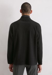 Schwarze Jacke mit strukturierter Oberfläche und geradem Schnitt, ausgestattet mit Kragen und langen Ärmeln. Glatter Stoff, schlichtes Design, sichtbare Naht am Rücken.