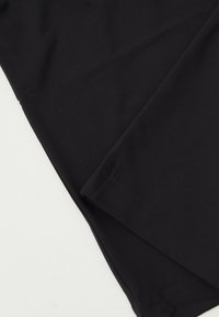 Κοντινό πλάνο από μαύρο ύφασμα διπλωμένο διαγώνια σε λευκό φόντο, που δείχνει λείο υφή και καθαρές άκρες.