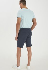 Tricou bărbați de culoare albastru deschis și pantaloni şort bleumarin, cu o textură netedă. Pantalonii şort au buzunare la spate și un croi drept. Adidași albi completează look-ul.