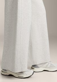 Helle graue weite Hosen mit gerippten Seitendetails, kombiniert mit hellgrauen Sneakers mit strukturiertem Obermaterial und schwarzer Sohle.