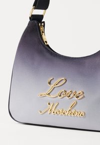 Satinasta torba s gradijentom od tamno do svijetlo ljubičaste boje, s zlatnim natpisom "Love Moschino" i zatvaranjem na patentni zatvarač. Mekana tekstura.