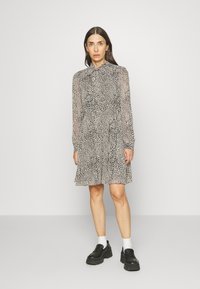 Vestido com padrão de onça, mangas longas transparentes, gola com babados e bainha rodada. Combinado com sapatos pretos robustos e meias brancas.