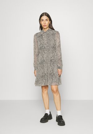 Vestido com padrão de onça, mangas longas transparentes, gola com babados e bainha rodada. Combinado com sapatos pretos robustos e meias brancas.