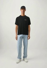 Juodas medvilninis marškinėliai su trumpomis rankovėmis, turintis mažą raudoną logotipą. Derinami su šviesiai mėlynomis tiesiomis džinsomis ir baltais sportbačiais.