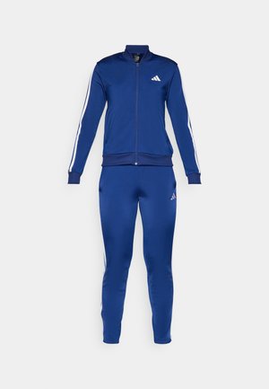 Blauer Sportanzug aus glattem Material; mit weißen Streifen an Ärmeln und Seiten, Reißverschlussjacke und eng geschnittenen Hosen.