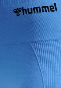 Blå sportleggings med ribbad midja och slät yta med en svart "hummel"-logotyp. Tillverkade av elastiskt tyg.