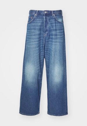 Bredde ben blå denimjeans med slitt vask, fem lommer og knappelukking. Glatt tekstur med subtil fading ved kneene.
