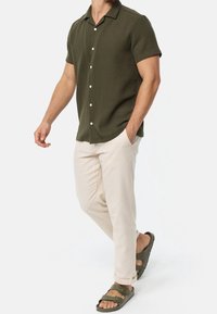 Korte mouwen, olijfgroene button-up shirt van een gestructureerde stof, gecombineerd met lichtbeige broek en donkergroene sandalen.