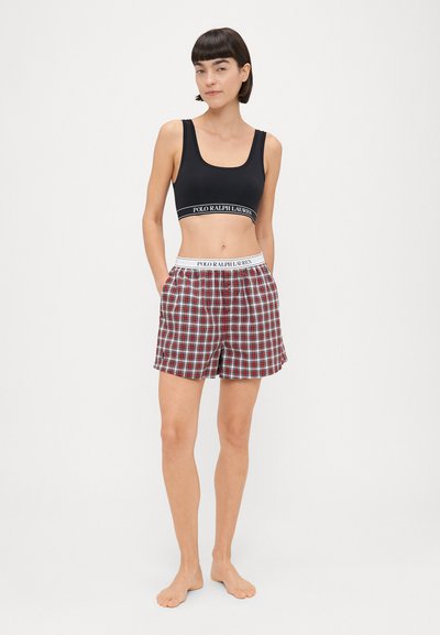 Μαύρο αθλητικό σουτιέν με λογότυπο στη ζώνη και κόκκινες μπλε σορτς με λευκή ελαστική μέση. Λείος ύφασμα, χαλαρή εφαρμογή και μέχρι το γόνατο.