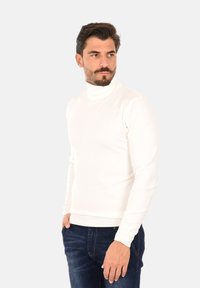 Maglione bianco a collo alto con design aderente, realizzato in un materiale morbido, con polsini e orlo a coste, abbinato a jeans blu scuro.