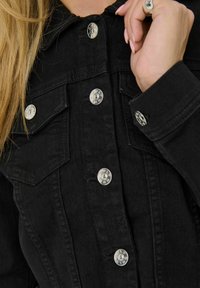 Black denim jacket with silver snap buttons, double chest pockets, and a collar. Fabric shows a smooth texture with slight fading.