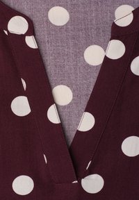 Tissu violet profond avec de grands pois blancs et un décolleté en V mettant en valeur un tissu violet plus clair avec de petits pois en dessous.