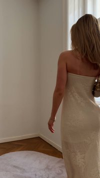 Gebreide buisjurk in beige met een bloemmotief, getailleerde pasvorm en een textuurafwerking. Draagt met een kleine handtas, gezet in een lichte kamer.