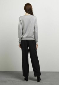 Grijze sweatshirt met lange mouwen en een relaxte pasvorm, met ribben bij de mouwen en onderkant; gecombineerd met zwarte wijde broek met een zijvak.