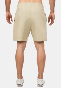 Pantaloni corti beige con vita elasticizzata e tasche laterali, realizzati in tessuto liscio e leggero, con una linea dritta e senza motivi visibili.