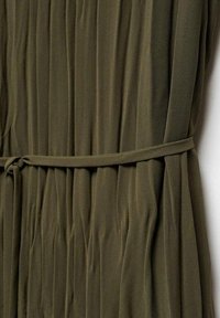 Oliivinvihreä laskostettu kangas, jossa on teksturoidun näköinen pinta ja vyötäröllä solmittu vyö istuvaa siluettia varten.