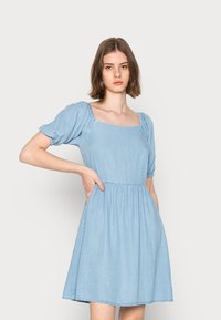 Vestido de ganga azul claro com mangas curtas balonê, decote quadrado, cintura franzida e saia rodada. Apresenta detalhes de costura visíveis.