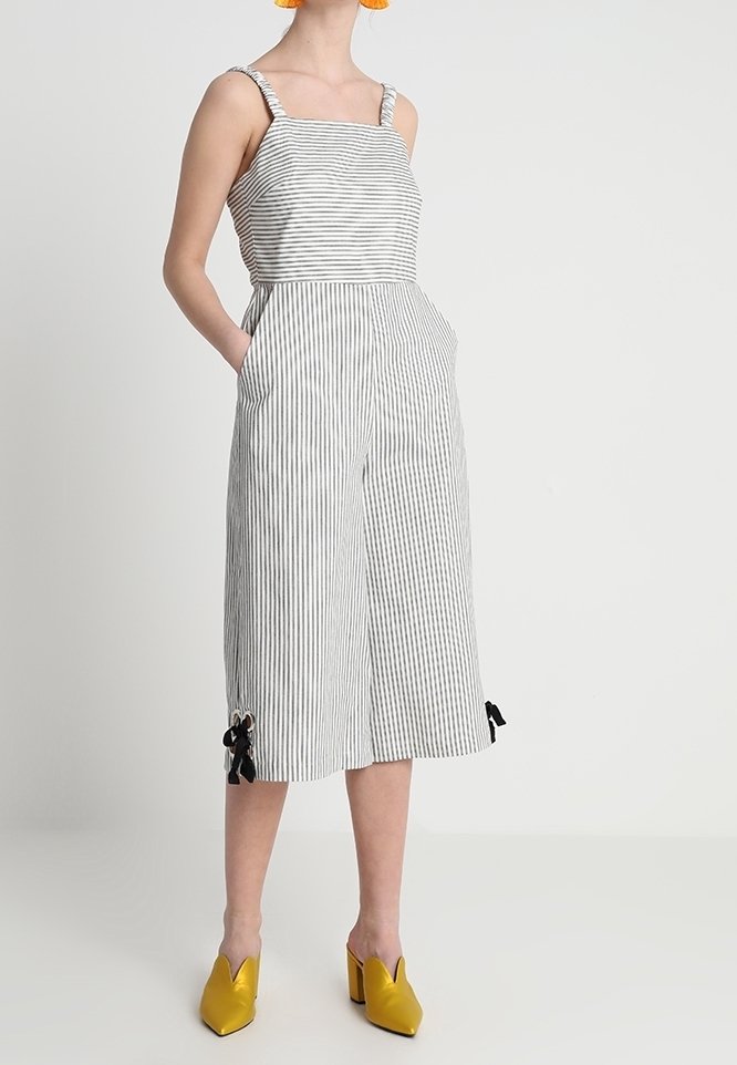 Combinaison rayée noire et blanche, dotée d'un col carré, de jambes larges, de poches latérales et d'accents de nœuds à l'ourlet. Chaussures jaunes.