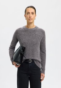 Pelēks vilnas džemperis ar garām piedurknēm, apaļu kakla izgriezumu un sānu spraugām, apvienots ar augsto jostasvietu tumšajām džinsām un matētu melnu rokassomu.