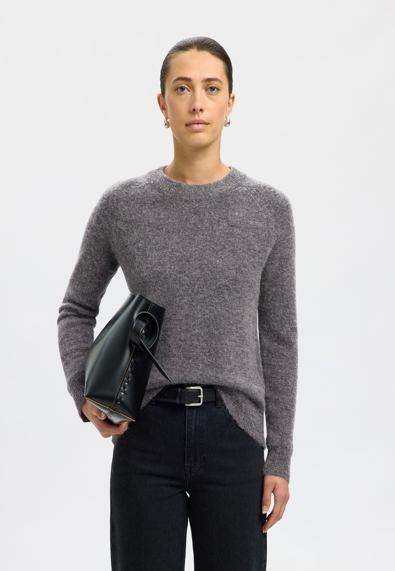 Pelēks vilnas džemperis ar garām piedurknēm, apaļu kakla izgriezumu un sānu spraugām, apvienots ar augsto jostasvietu tumšajām džinsām un matētu melnu rokassomu.