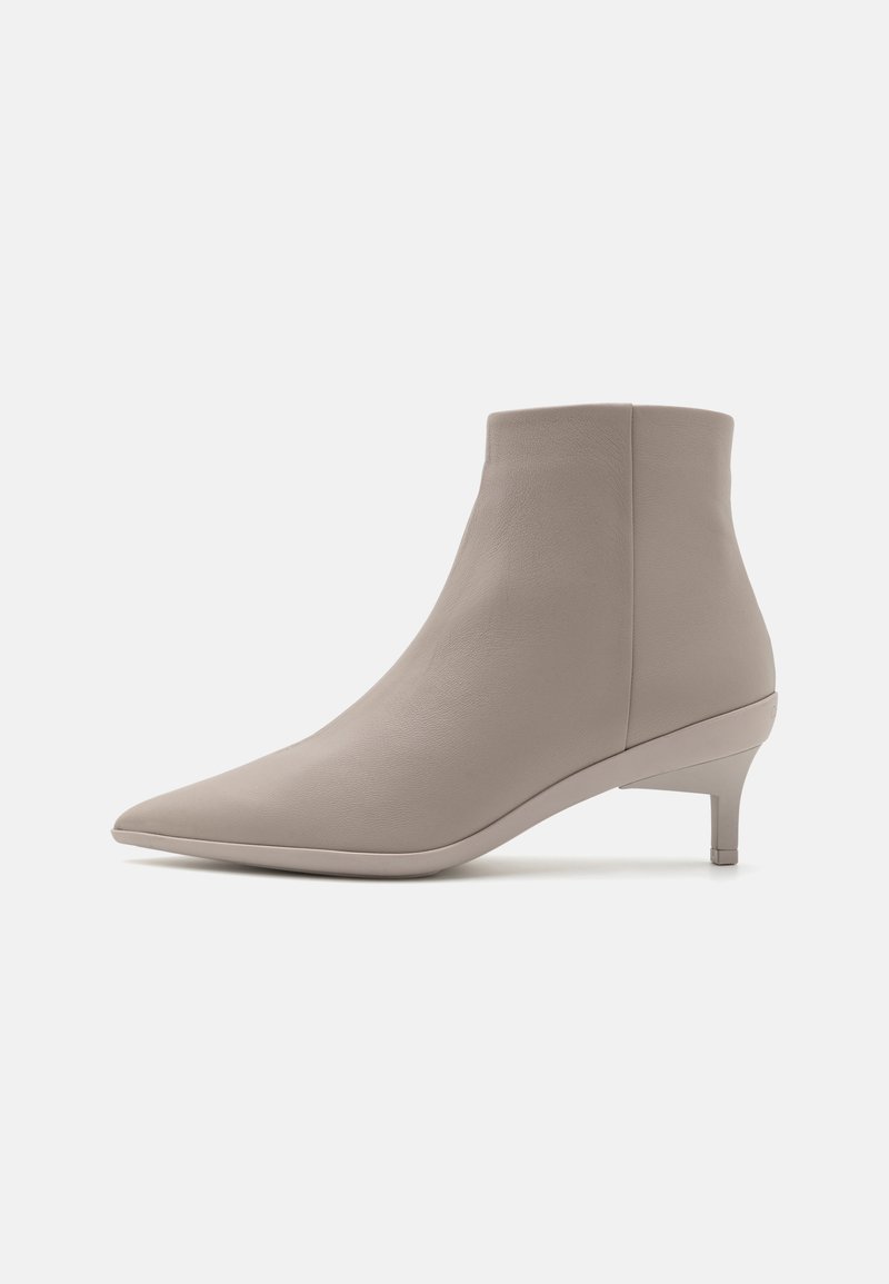 Botín de cuero beige hasta el tobillo con punta afilada y tacón delgado. Textura suave y diseño minimalista sin herrajes o patrones visibles.