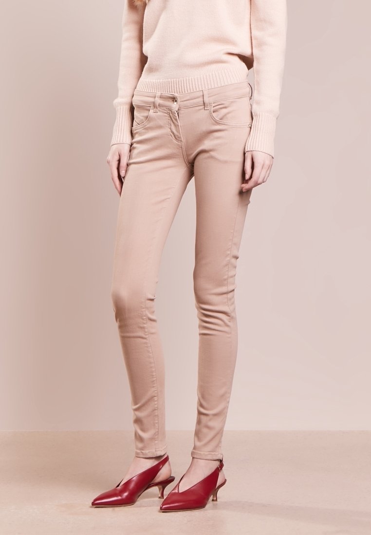 Beige skinny džíny vyrobené z bavlněné směsi, s mírným vzestupem pasu, předními kapsami a hladkou texturou. V kombinaci s červenými lodičkami na podpatku.