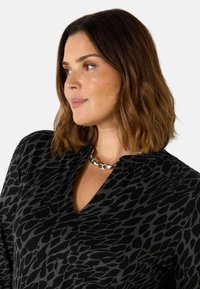 Černá blůza s leopardím vzorem v šedých odstínech, s výstřihem do V a krátkými rukávy. Obsahuje stříbrný kulatý řetízek.