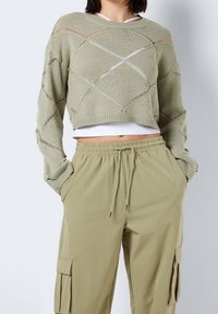 Ljusgrön kort tröja med diamantstickmönster och öppna nätdetaljer, kombinerad med olivgröna cargobyxor med elastiskt midjeband och fickor.