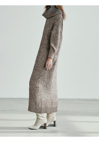 Robe longue en tricot dans des tons marron et beige, dotée d'un col roulé côtel é haut et de manches longues, associée à des bottines blanches à la cheville avec un talon en bois.