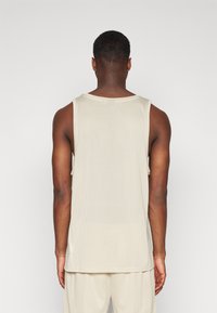 Débardeur en maille beige sans manches, à coupe décontractée et col rond, avec un motif texturé et un ourlet droit, conçu pour la respirabilité.