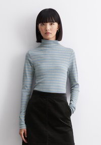 Langarm-Turtleneck in Hellblau mit dunklen horizontalen Streifen; weicher Stoff mit glatter Textur; getragen mit einem schwarzen Cordrock.