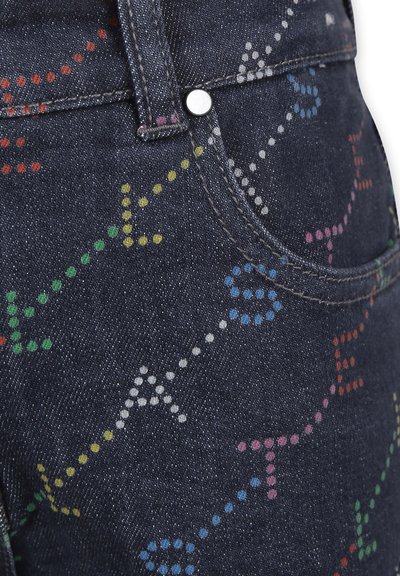 Jeans in denim scuro con motivi a pois multicolori in varie forme, tra cui frecce, cerchi e linee. Visibile dettaglio del bottone argentato.